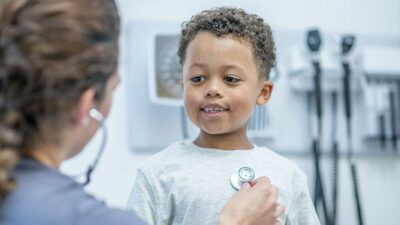 doctor listens to heart beat of happy young boy during medical exam