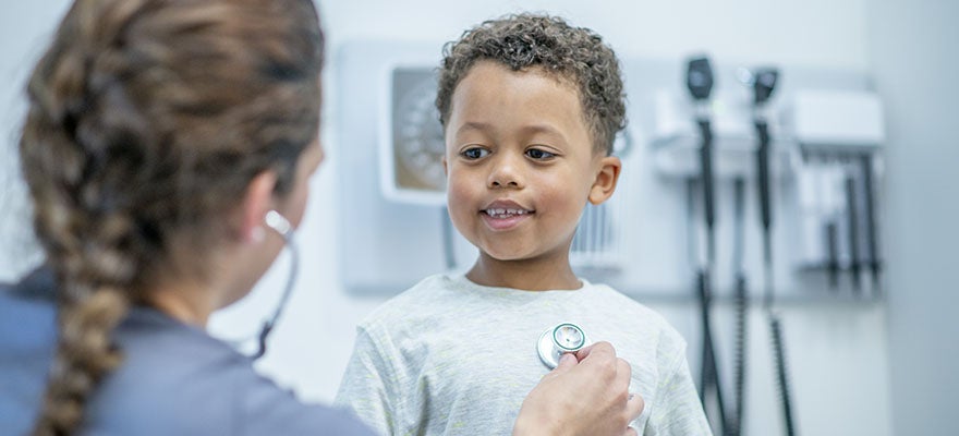 doctor listens to heart beat of happy young boy during medical exam