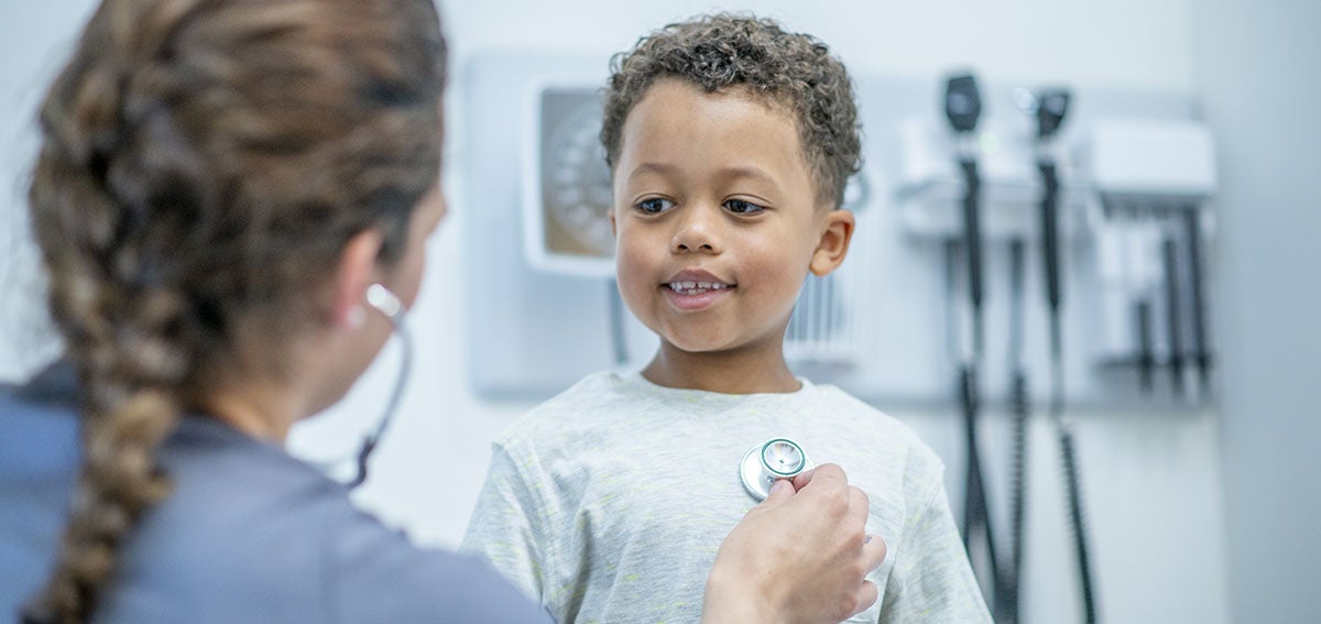 doctor listens to heart beat of happy young boy during medical exam