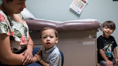 Mother and two young children wait in clinic exam room.