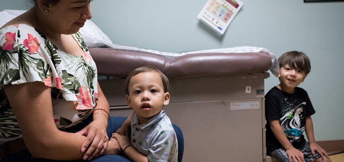 Mother and two young children wait in clinic exam room.