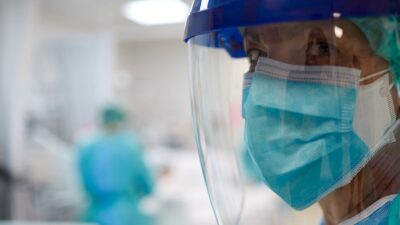 Medical professional in hospital room, wearing multiple masks and face shield