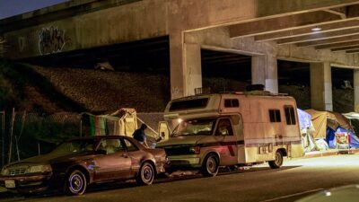 Vehicles sit parked next to tents beneath the overpass of U.S. Highway 101 in Los Angeles, California.