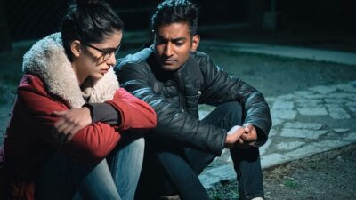 Man and woman sitting on sidewalk at night, having a serious conversation/counseling
