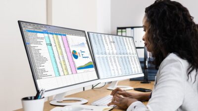 Doctor working on a spreadsheet using two computer monitors