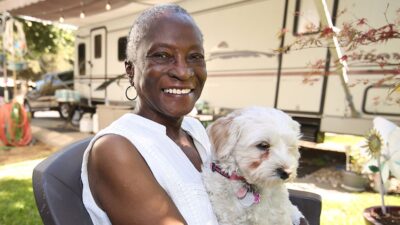 Woman sitting outside of her home with a small dog in her lap.