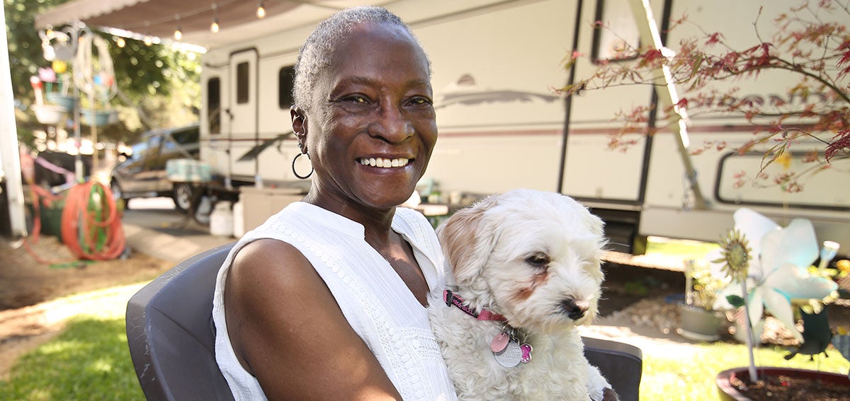 Woman sitting outside of her home with a small dog in her lap.