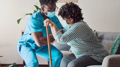health care provider helping elderly woman stand up from sitting