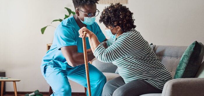 health care provider helping elderly woman stand up from sitting