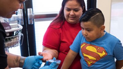 Boy watches with interest as mother gets blood glucose test