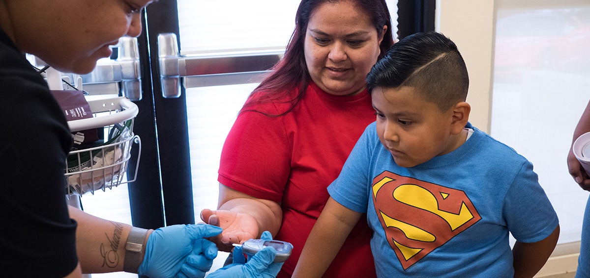 Boy watches with interest as mother gets blood glucose test