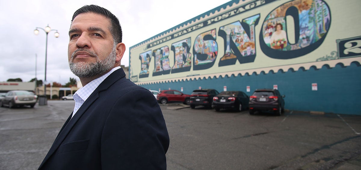 Joe Prado standing in front of "Fresno" mural