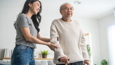 young woman helping elderly man with a cane walk