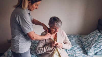 Younger women helps older woman put on sweater.