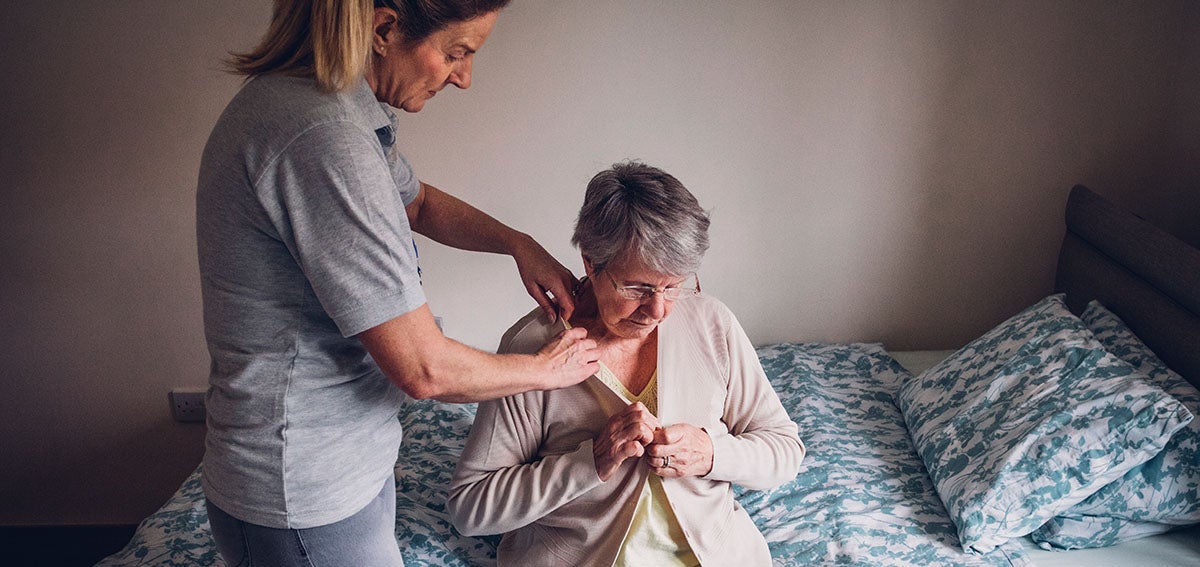 Younger women helps older woman put on sweater.