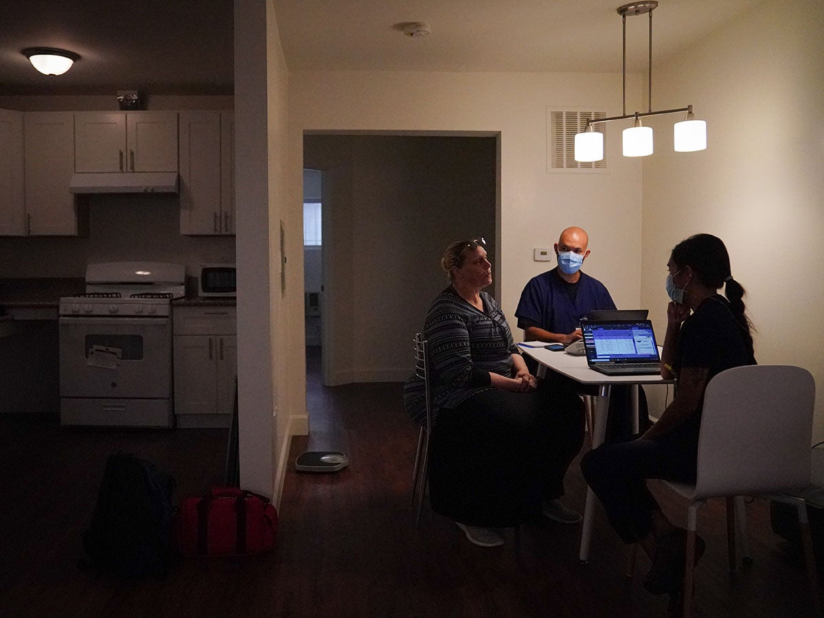 Three people sit in kitchen of new apartment.