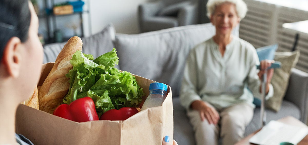 Assisted living caregiver delivers groceries to woman at home.