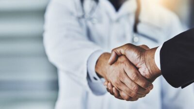 Doctor shaking hands with person wearing suit.