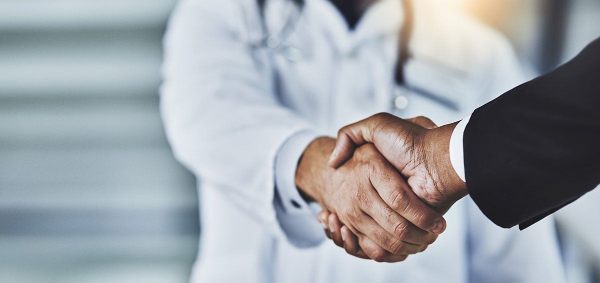 Doctor shaking hands with person wearing suit.