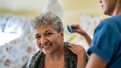 Elderly woman having her hair styled by an in-home aid.