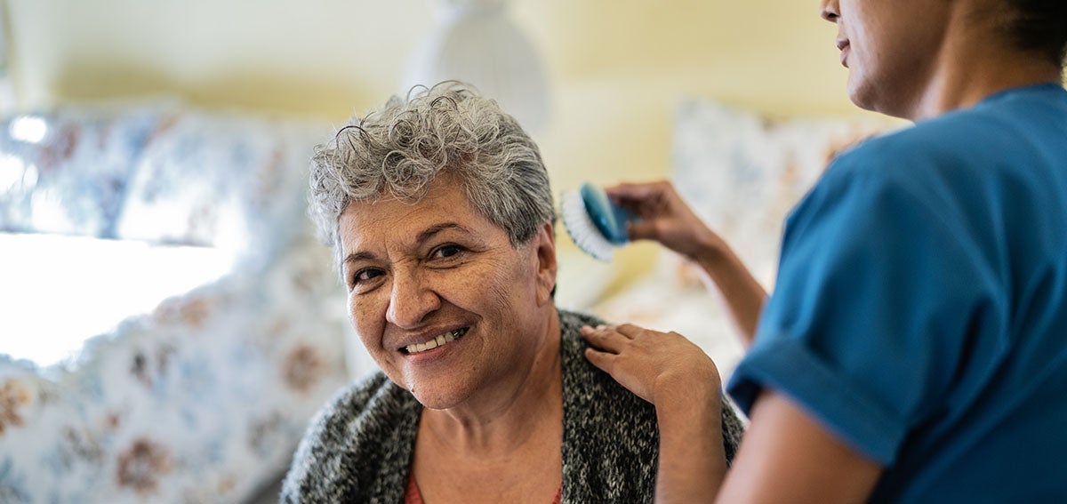 Elderly woman having her hair styled by an in-home aid.