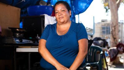 Woman experiencing homelessness sits under a tarp with her belongings.