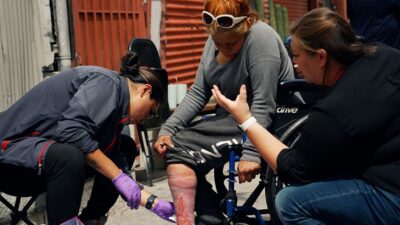 Street medicine team cleans wound on the leg of a woman experiencing homelessness.