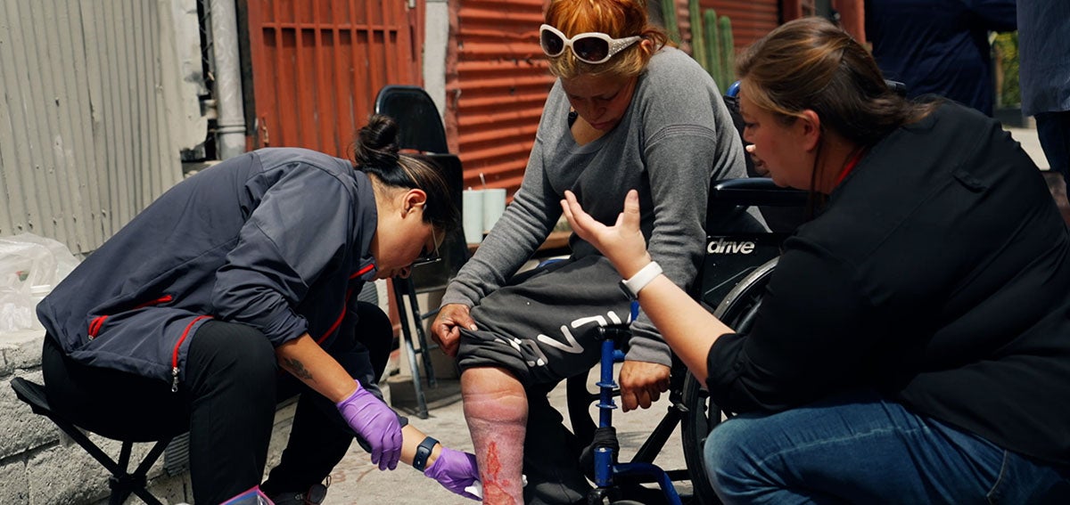 Street medicine team cleans wound on the leg of a woman experiencing homelessness.
