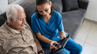 Home health care worker shows patient information on a tablet.