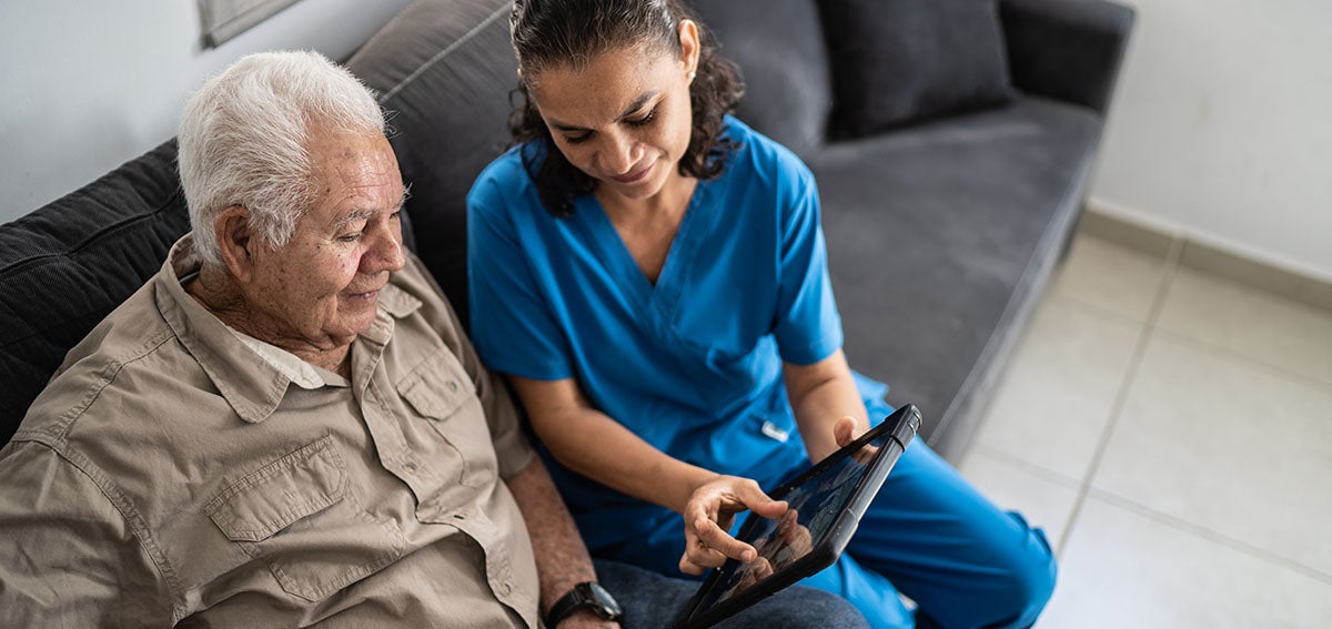 Home health care worker shows patient information on a tablet.