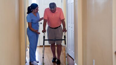 Medical practitioner helps man using a walker at home