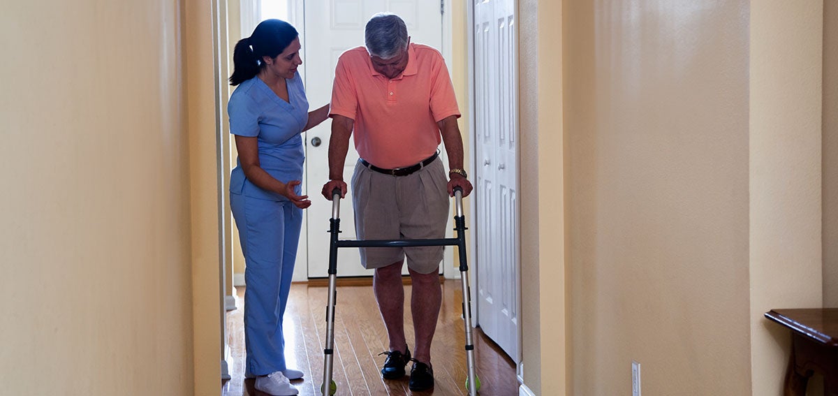 Medical practitioner helps man using a walker at home