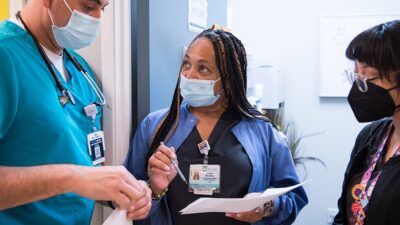 Three health care workers haveing a conversation in clinic hallway.
