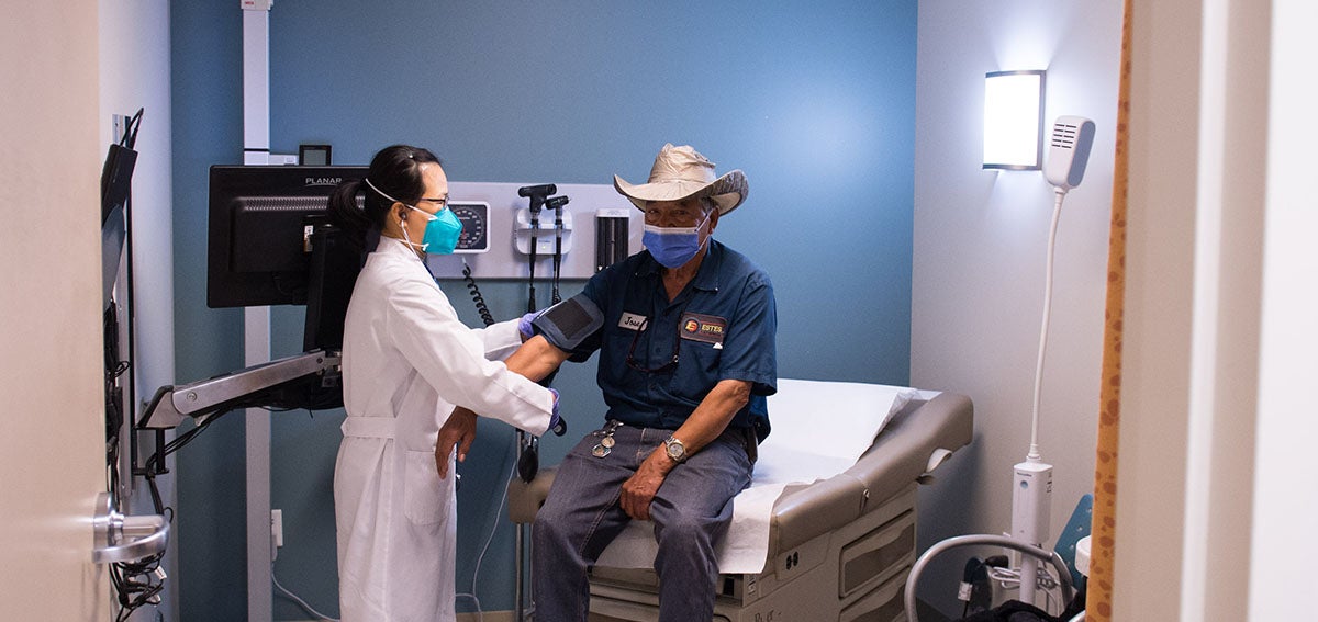 A man is seated on an exam table in a clinic being examined by a physician as California moves closer to health equity