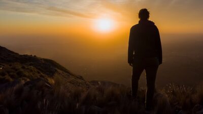 Person standing on hill looking at sun