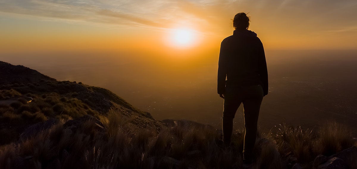 Person standing on hill looking at sun