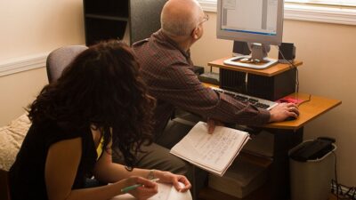 A man works at a computer while his co-worker looks on
