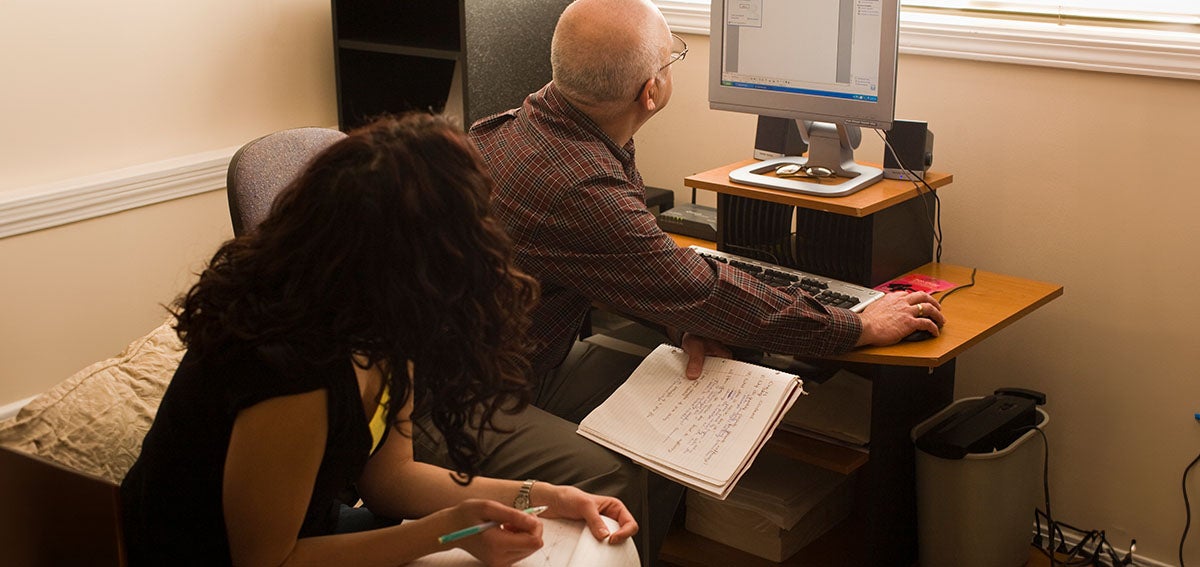 A man works at a computer while his co-worker looks on
