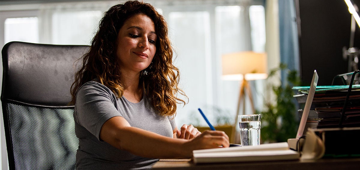 Woman sitting at desk with computer and writing materials