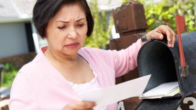 Woman standing at mailbok looking at letter with concerned expression on her face