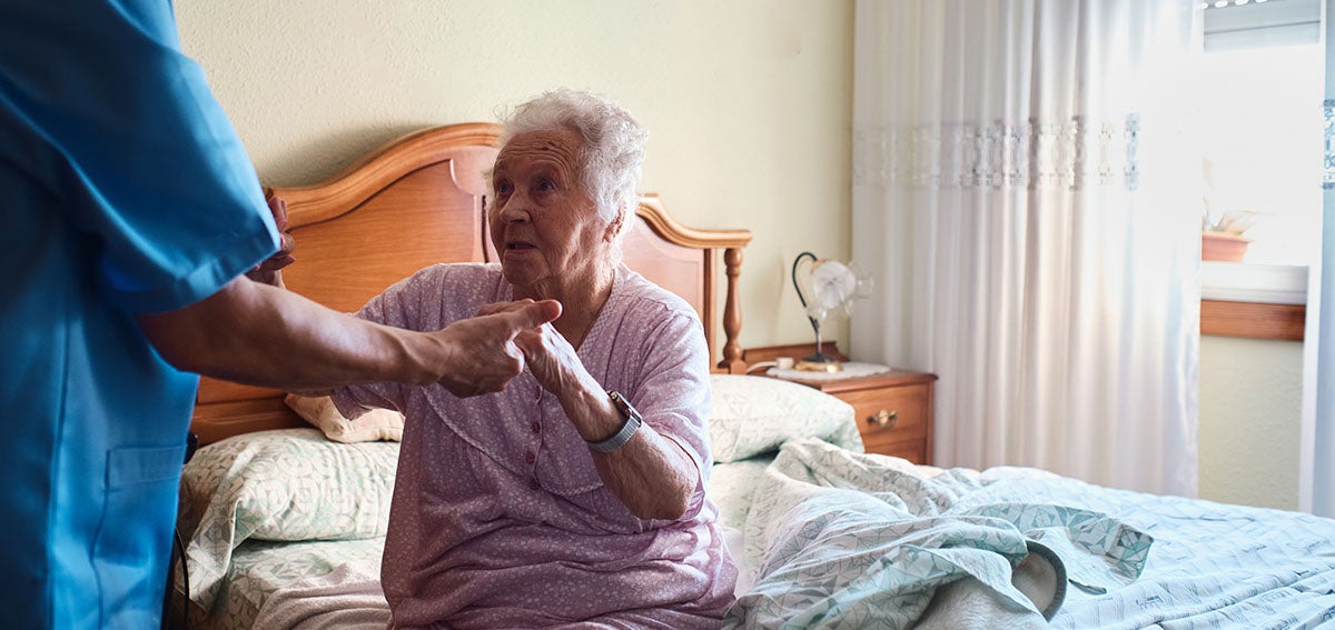 Home health aide helps elderly woman rise from bed