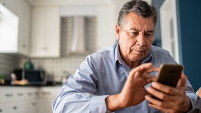 Older man sitting in kitchen, texting.