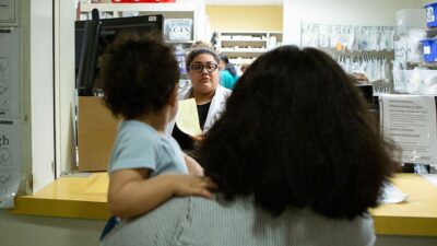 Woman holding small child speaks to Pharmacist