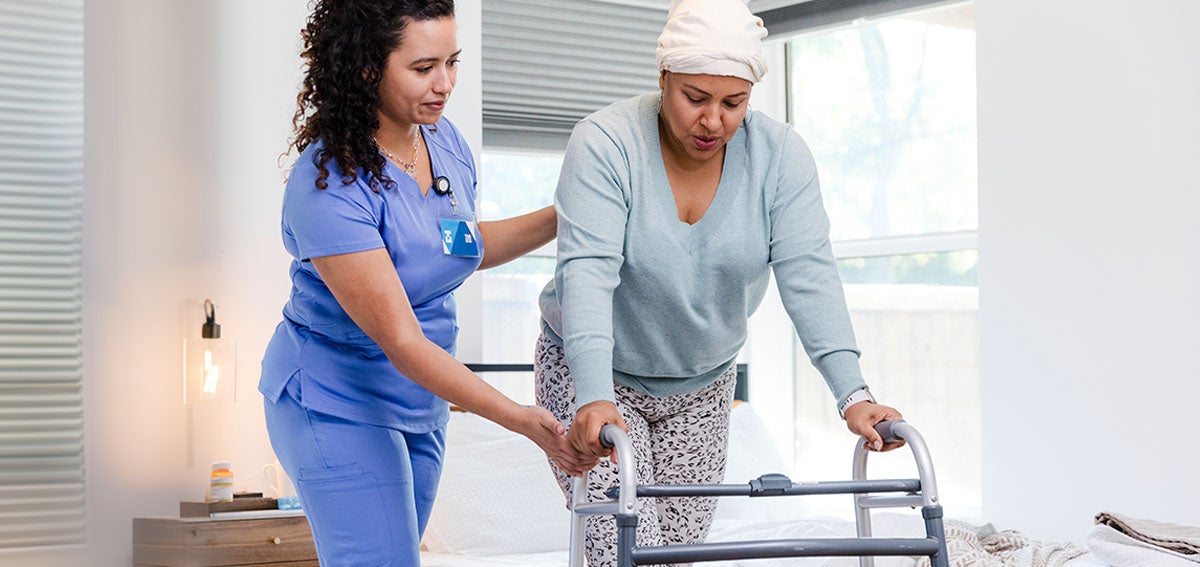 Medical practitioner helps patient walk with assistive device.