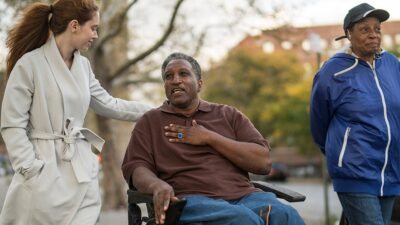 Young woman, older man in wheelchair, older woman walking