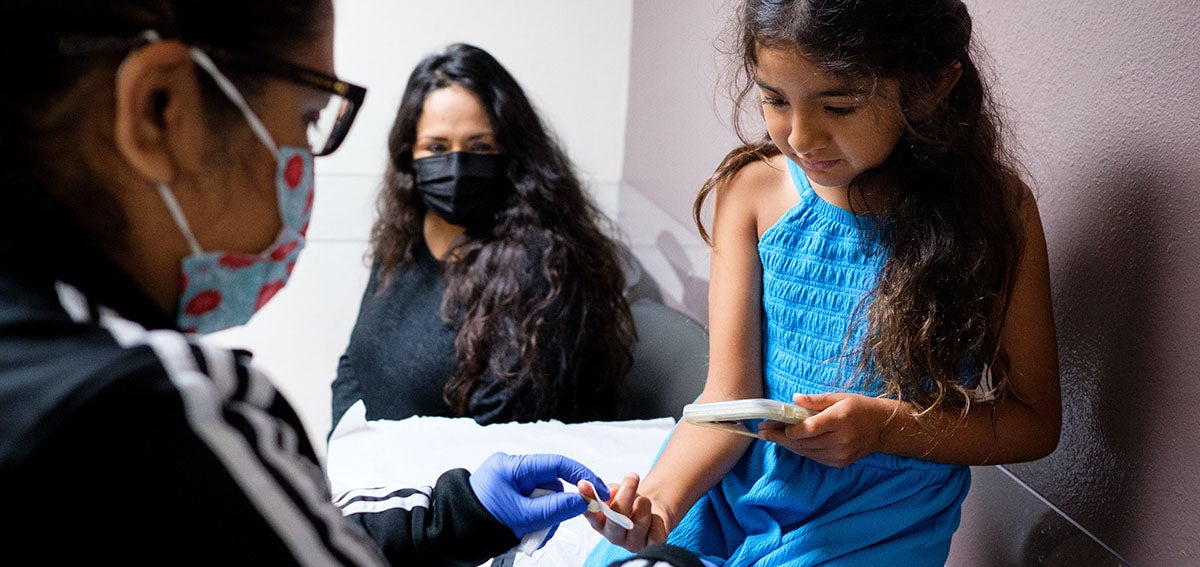 Trump Cuts Could Hurt Medi-Cal - threats to federal assistance Mother and daughter at a medical clinic with doctor.