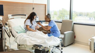 Midwife talks to new mother holding baby in the hospital.