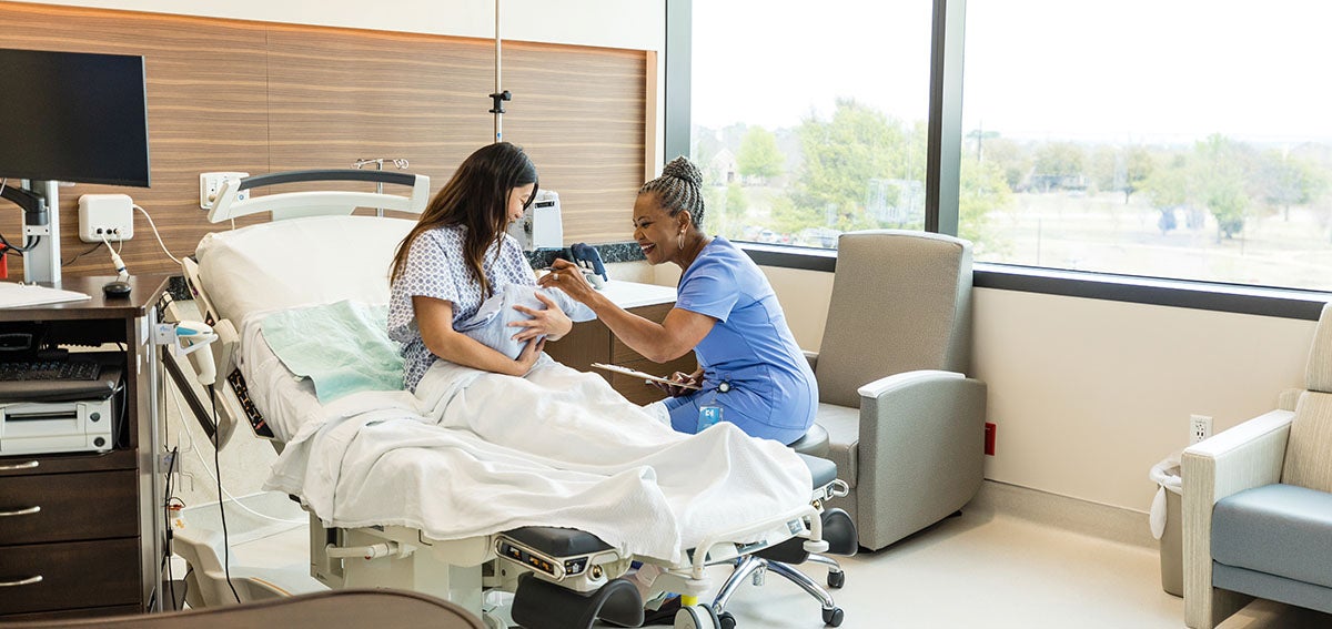 Midwife talks to new mother holding baby in the hospital.