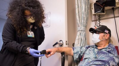 Medical assistant checks pulse on elderly patient in the clinic.