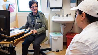Doctor talks to Patient twhile endtering information into an Electronic Medical Record.,